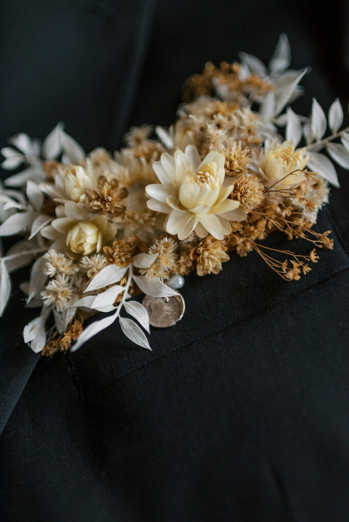 A close up shot of a boutonnière with cream & neutral florals and a fingerprint charm from a Cades Cove wedding in TN